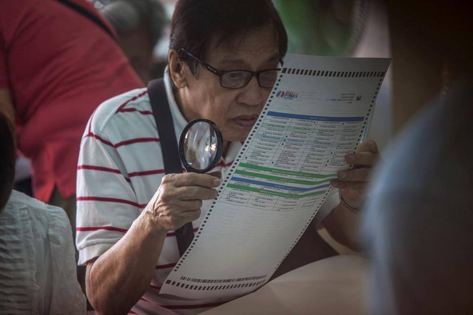 An elderly man uses a magnifying glass to read and fill out his ballot at the Sta. Lucia Elementary School in San Juan. Photo by LUIS LIWANAG