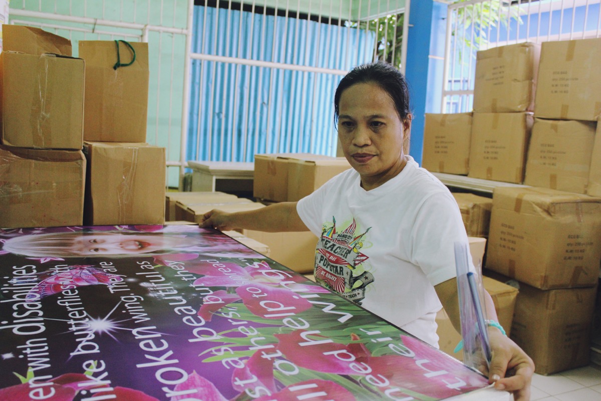 Maria Theresa Marquina puts a tarpaulin with quote for children with disabilities on a Styrofoam board before hanging it on the special education (SPED) center's wall. Photo by ARIANNE CHRISTIAN TAPAO