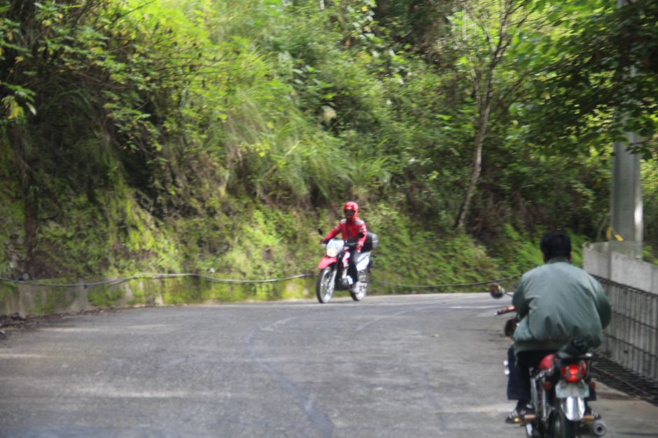 One road, two motorcycle riders: one with a helmet, the other without