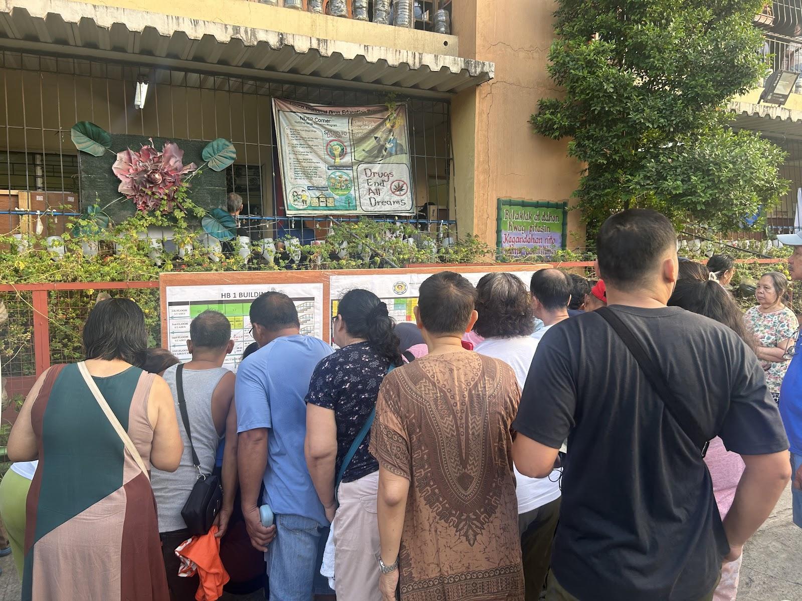 Voters crowd around the list of precinct assignments at President Corazon C. Aquino Elementary School in Quezon City.